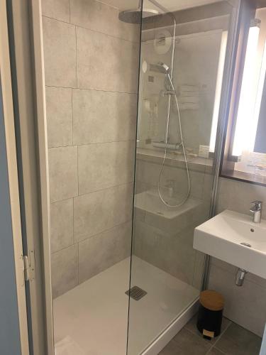 a shower with a glass door next to a sink at The Originals City, Hôtel Le Gayant, Douai in Douai