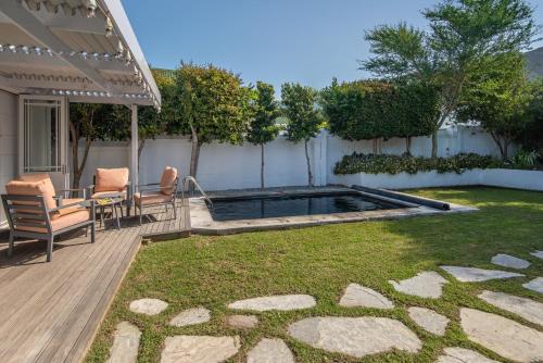 a backyard with a pool and a deck with chairs at Cosy Cottage Onrus - With Pool in Hermanus