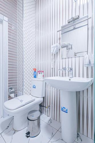 a white bathroom with a toilet and a sink at Merhaba Hotel, Fergana in Fergana