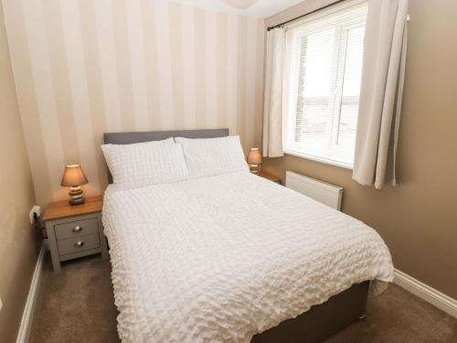 a bedroom with a white bed and a window at Twyni Bach in Burry Port