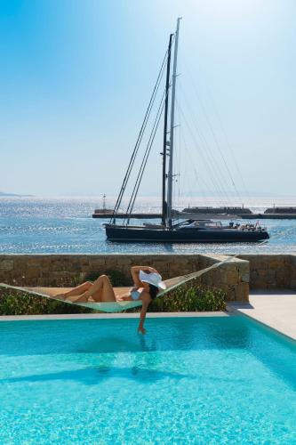 a woman in a swimming pool next to a sailboat at Mykonos Riviera Hotel & Spa, a member of Small Luxury Hotels of the World in Tourlos