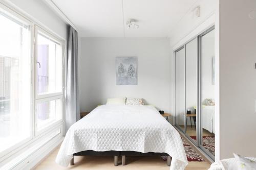 a white bedroom with a bed and large windows at Moderni avara yksiö Jyväskylän ydinkeskustassa in Jyväskylä