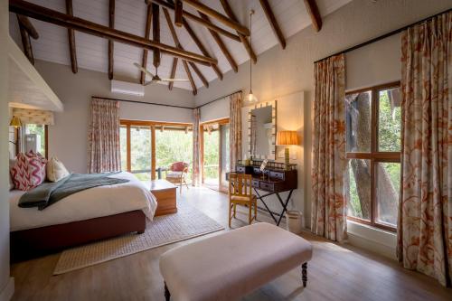 a bedroom with a bed and a desk and windows at Shimungwe Lodge, Thornybush Game Reserve in Hoedspruit