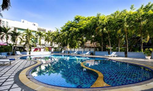 a large swimming pool with chairs and trees at Sawasdee Siam Pattaya Hotel in Pattaya