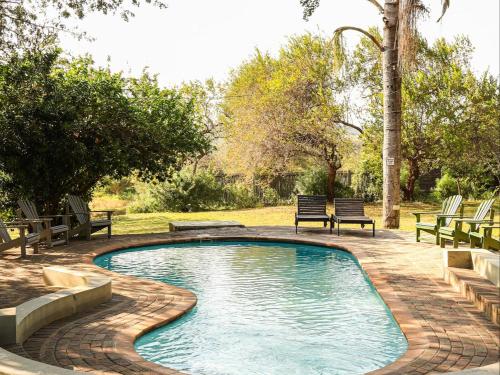 a swimming pool with benches around it in a yard at Kruger Foothills Lodge - Near Kruger National Park in Hoedspruit