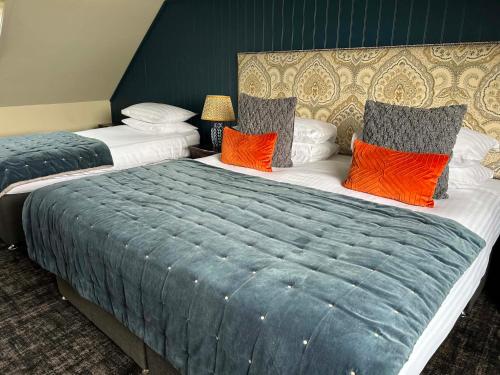 two beds in a hotel room with orange pillows at Lochside Hotel in Bowmore