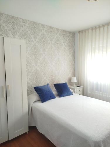 a bedroom with a large white bed with blue pillows at Pensión Vegadeo GIJÓN in Gijón