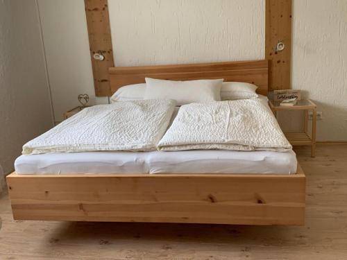 a wooden bed with white sheets and pillows at Ferienwohnung "Zirbenduft" im Landhotel Seeg in Seeg