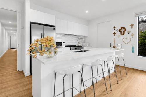 a white kitchen with a large white counter with stools at Albert Samian Retreat by Ready Set Stay - BYO sheets and towels in Capel Sound