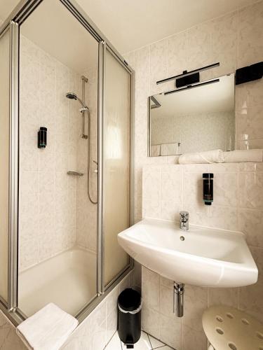 a white bathroom with a sink and a shower at Hotel Schillerbad in Lüdenscheid