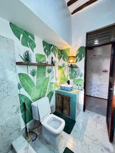 a bathroom with a toilet and a mural of leaves at FURAHA GARDEN Rooms in Kendwa