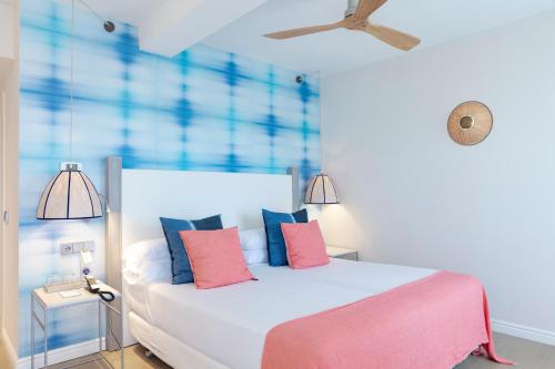 a bedroom with a white bed with pink and blue pillows at Hotel Honucai in Colònia de Sant Jordi