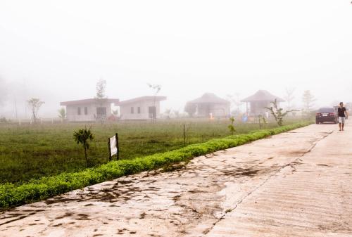 a man walking down a dirt road in front of houses at Santitham Home Farm Stay in Mae Taeng
