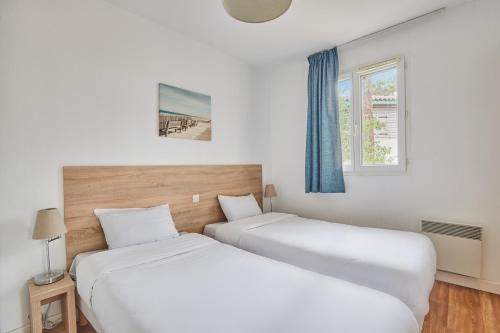 two beds in a room with two windows at Résidence Odalys Bleu Ocean in Moliets-et-Maa