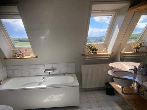 a bathroom with a tub and a sink and two windows at Main House - Rolsø Retreat in Knebel