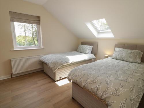 two beds in a bedroom with two windows at Brook Cottage in Coleraine