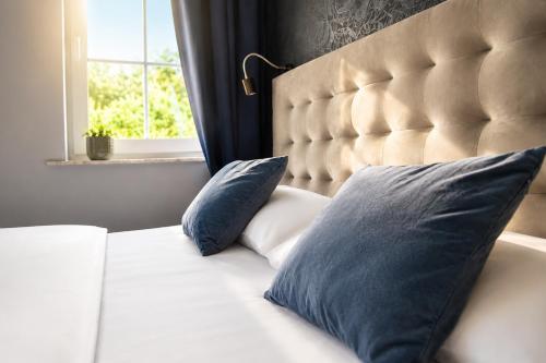 a bed with two blue pillows and a window at Hotel Kornblume in Haundorf
