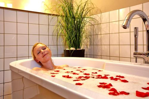 una mujer tumbada en una bañera con pétalos rojos en relexa hotel Harz-Wald Braunlage GmbH, en Braunlage