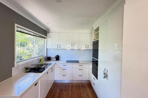 a white kitchen with white cabinets and a window at Pool house for BIG Groups with Free parking in Marsden