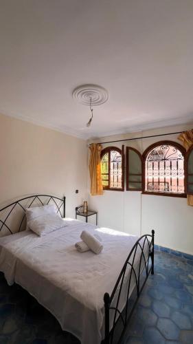 a bedroom with a bed with white sheets and two windows at Moana Guest House in Tamraght Ouzdar