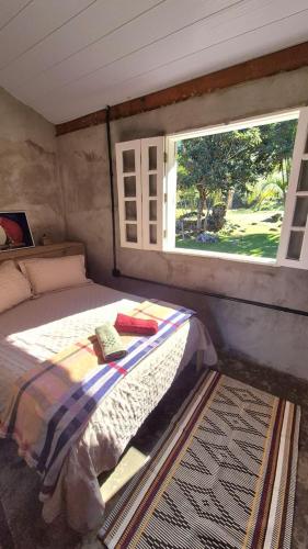 a bedroom with a bed with a window and a rug at Chalé Joanópolis - Rancho da Biruta in Joanópolis