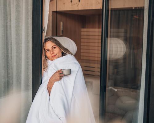 a woman in a robe holding a cup of coffee at Anton & Cilli Hideaway Lodges in Obermaiselstein