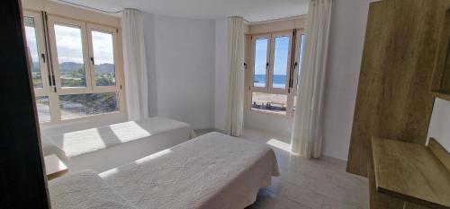 a white room with two beds and two windows at Apartamentos Regollera in Noja
