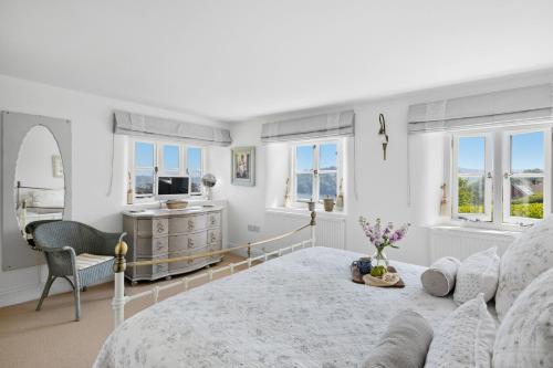 a white room with a bed and a desk and windows at Dart View Cottage - A Stunning Riverside Escape in the Heart of South Devon in Dittisham