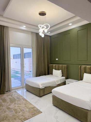 two beds in a room with green walls and a chandelier at شالية ماربيا الاشخرة Marbella Ashkhara Chalet in Al Sharqiyah