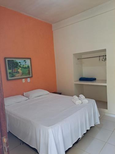 a bedroom with a white bed and an orange wall at Pousada Coqueiro Verde in Mateus Leme