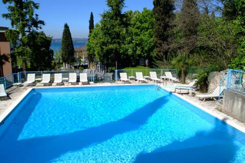 uma piscina com água azul e cadeiras brancas em Hotel Broglia em Sirmione