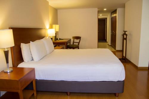 a bedroom with a large white bed and a desk at Hotel Estelar Suites Jones in Bogotá