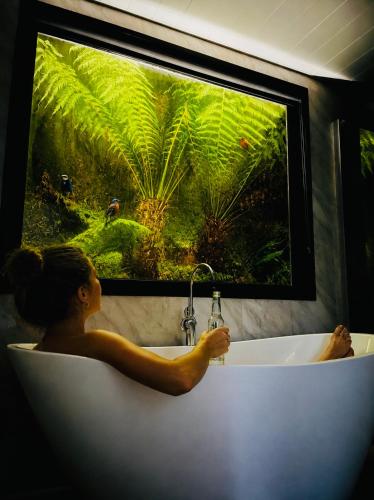 a woman sitting in a bath tub with a large window at The Cozy Cottage-With elevated views in Queenstown