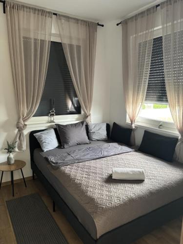 a bed in a bedroom with two windows at Lily Beach Apartman in Balatonlelle