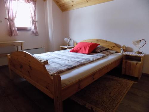 Apartment Zeleni dragulj Pohorje في Oplotnica: غرفة نوم بسرير خشبي ومخدة حمراء