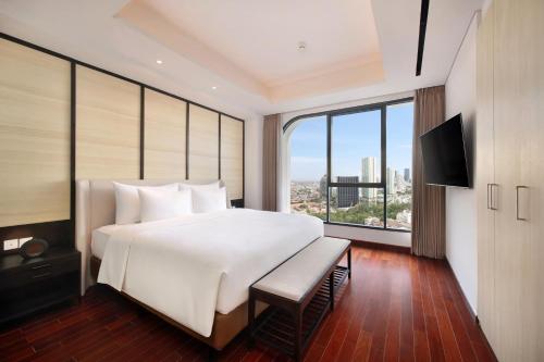 a bedroom with a large white bed and a large window at Vasa Suite Surabaya in Surabaya