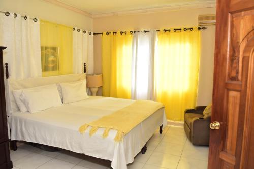 a bedroom with a large white bed and yellow curtains at Embassy Royale in Kingston