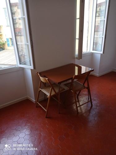 a wooden table and a chair in a room with windows at GautierNice in Nice