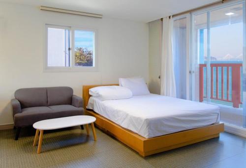 a bedroom with a bed and a chair and a window at Beachblue Pension Geoje in Geoje