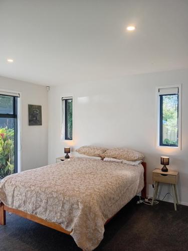 a bedroom with a large bed and two windows at Mangawhai Palms in Mangawhai