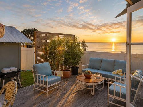 a patio with a couch and chairs and the ocean at Beachfront Bliss - Stay Waiheke in Onetangi
