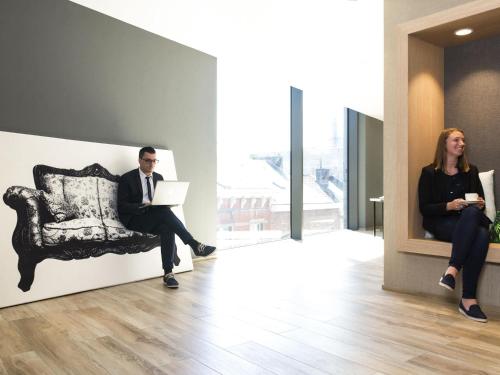 a man and a woman sitting in a chair with a laptop at Novotel Charleroi Centre in Charleroi