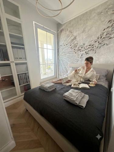 a woman sitting on a bed reading a book at Tesoro Dolce Vita Apartment in Pogórze