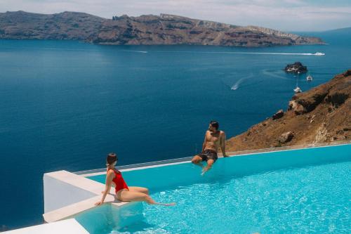 two people sitting on the edge of a swimming pool at Saint Santorini in Oia