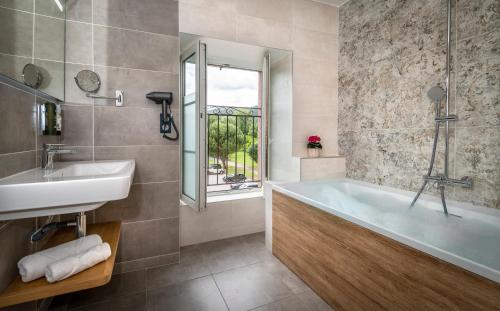 a bathroom with a tub and a sink and a window at Logis Hôtel Restaurant Les 2 Rives - CHAMBRES CLIMATISEES - A75, en bordure de rivière in Banassac