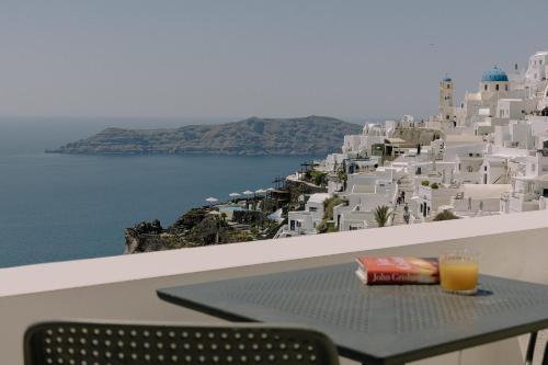 a table with a glass of orange juice sitting on a balcony at Agave Santorini Design Boutique Hotel in Imerovigli