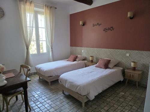 a bedroom with two beds and a table and window at Mas de la Bimarde in Monteux