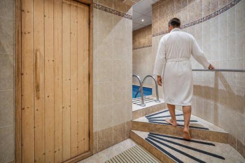 a man in a bathrobe standing in a bath tub at Hotel Adamantino in Luhačovice