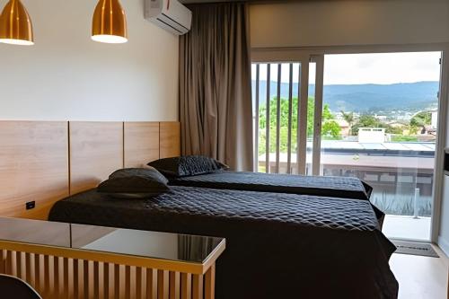 a bedroom with two beds and a large window at Condomínio Brises Downtown Garopaba in Garopaba