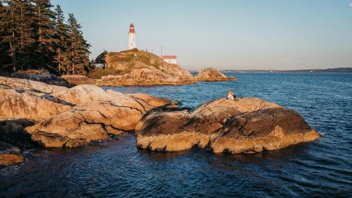 a person sitting on rocks in the water with a lighthouse at 2BD Guest Suite Sleeps 6 Near Downtown & Beach in West Vancouver